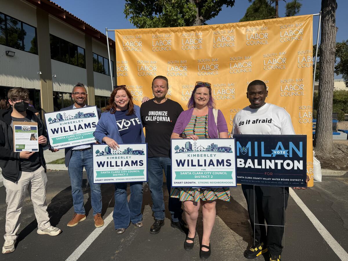 Milan Balinton with volunteers holding campaign signs in front of a South Bay Labor Council banner