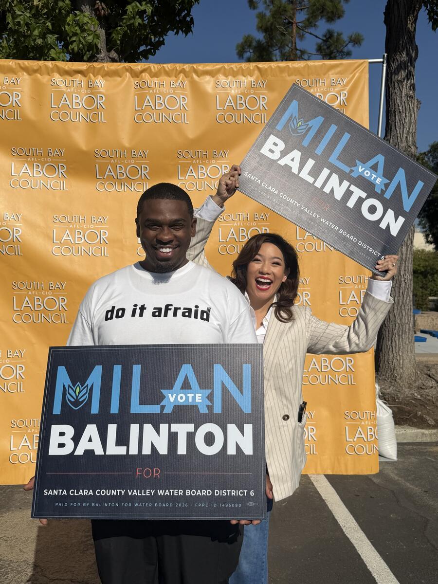 Milan Balinton holds a campaign sign as a supporter raises another sign behind him