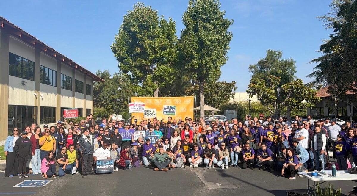 A large group of supporters gathers for a group photo in front of a South Bay Labor Council banner