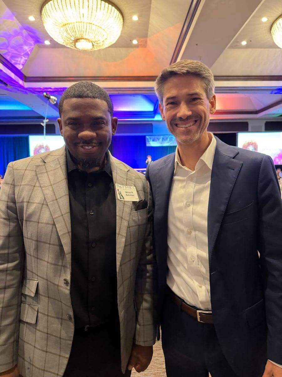 Milan Balinton with an event guest in a navy suit at a BAYMEC gathering